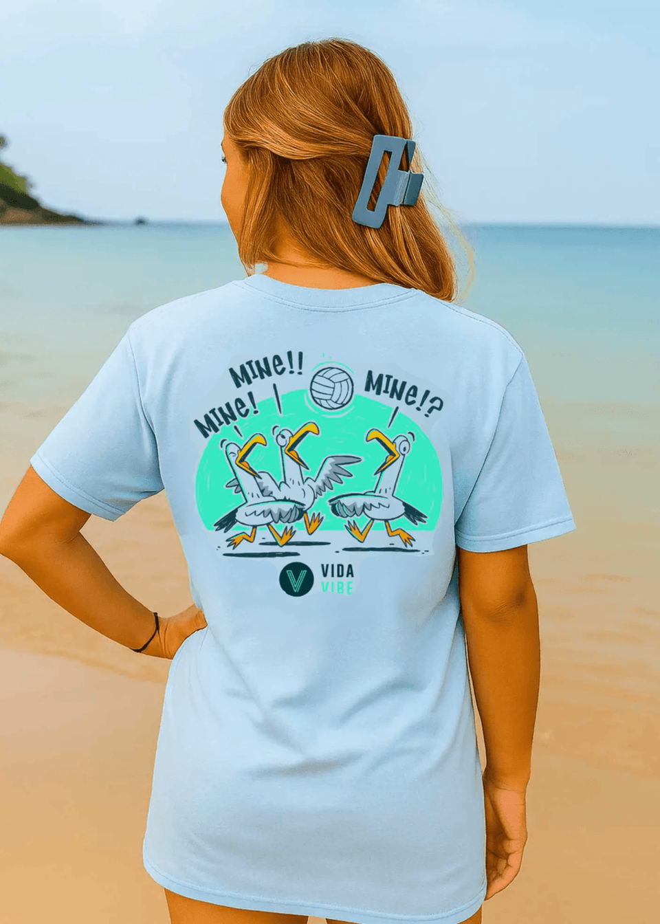 Person wearing a light blue t-shirt with a graphic design on a beach